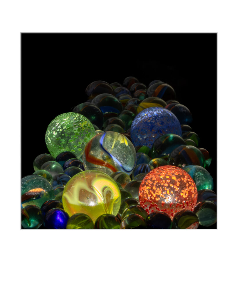 Une collection de billes de verre colorées, y compris de grosses billes vertes, jaunes, bleues et rouges avec des motifs complexes, présentées sur un fond noir.