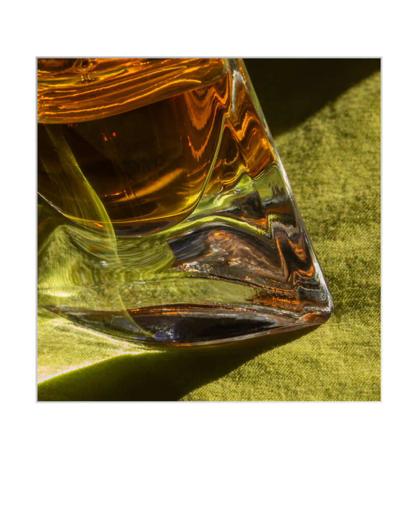 Gros plan d'un verre contenant un liquide ambré, peut-être du whisky, sur une surface texturée verte. La lumière et les reflets créent des motifs abstraits à travers la base du verre.
