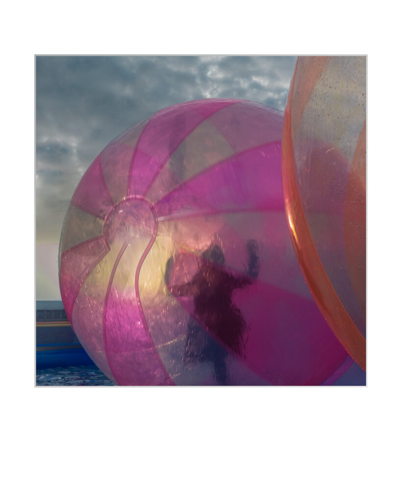 Une personne est visible en silhouette à l'intérieur d'un grand ballon gonflable rose translucide en plein air, avec en arrière-plan des nuages et des rayons de soleil spectaculaires.