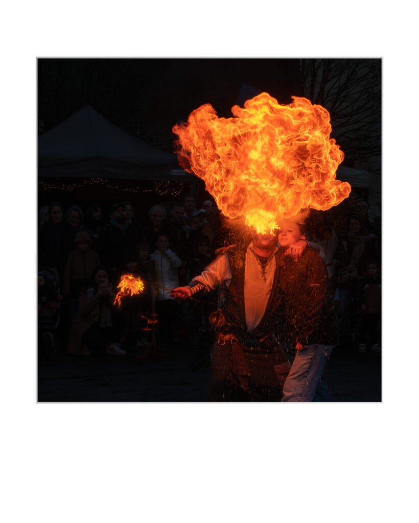 Un artiste de rue souffle un grand coup de feu dans l'air, divertissant une foule de spectateurs lors d'un événement en plein air dans la soirée.