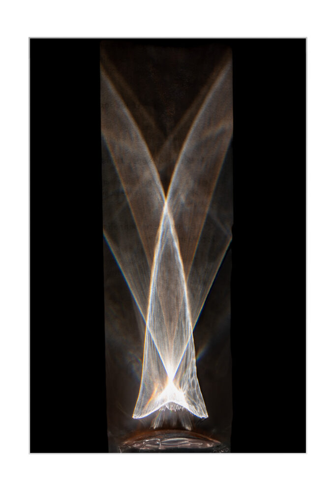 Des motifs lumineux blancs abstraits forment des arcs et des formes qui se croisent sur un fond sombre et vertical, créant un effet symétrique et éthéré qui ressemble à des ailes lumineuses ou à un papillon.