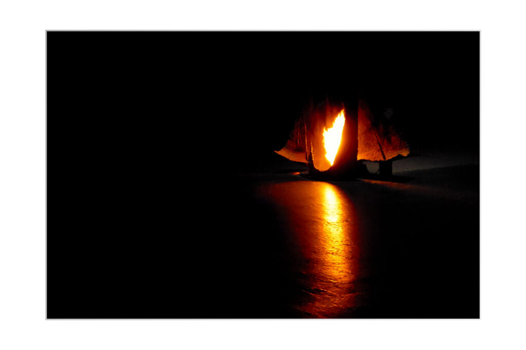 Une lumière orange incandescente brille sous un tissu sombre et drapé, projetant un reflet brillant sur le sol d'un espace par ailleurs très noir.