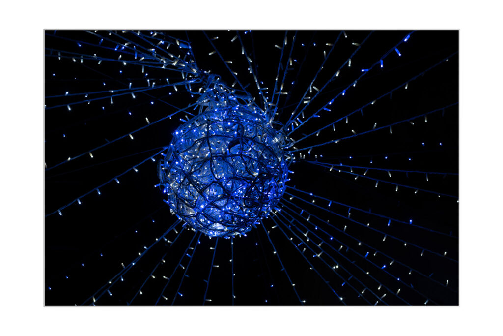 Une structure sphérique enveloppée de lumières bleues est suspendue sur un fond sombre, avec des fils de lumières bleues et blanches rayonnant dans toutes les directions.