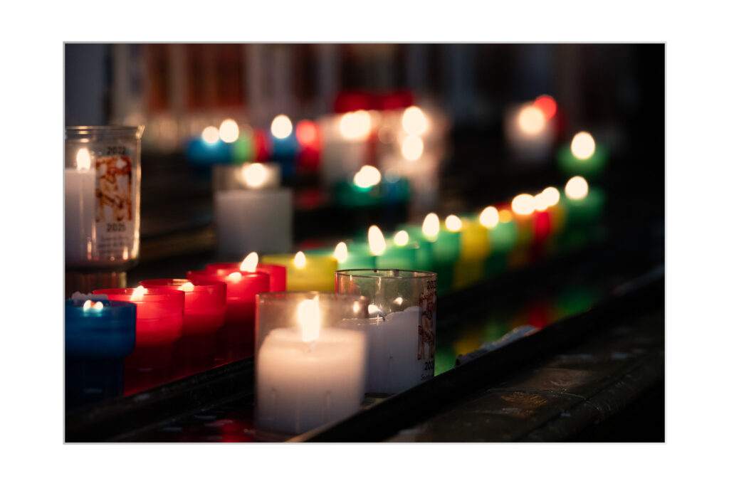 Basilique Sainte_Anne : Une variété de bougies colorées, notamment rouges, blanches, bleues, vertes et jaunes, sont allumées et disposées en rangées sur une surface sombre, créant une atmosphère chaleureuse et lumineuse.