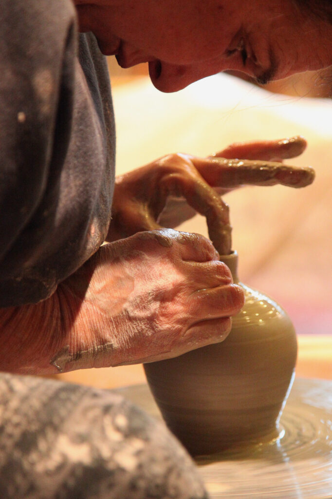 Une personne façonne avec soin un petit pot en argile sur un tour de potier, les mains recouvertes d'argile humide, tout en se concentrant intensément sur son travail.
