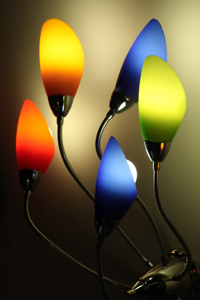 Cinq lampes modernes et modulables, dotées d'abat-jours colorés (rouge, jaune, vert et bleu), brillent de mille feux sur un mur uni, créant ainsi un jeu de lumières dynamique et artistique.