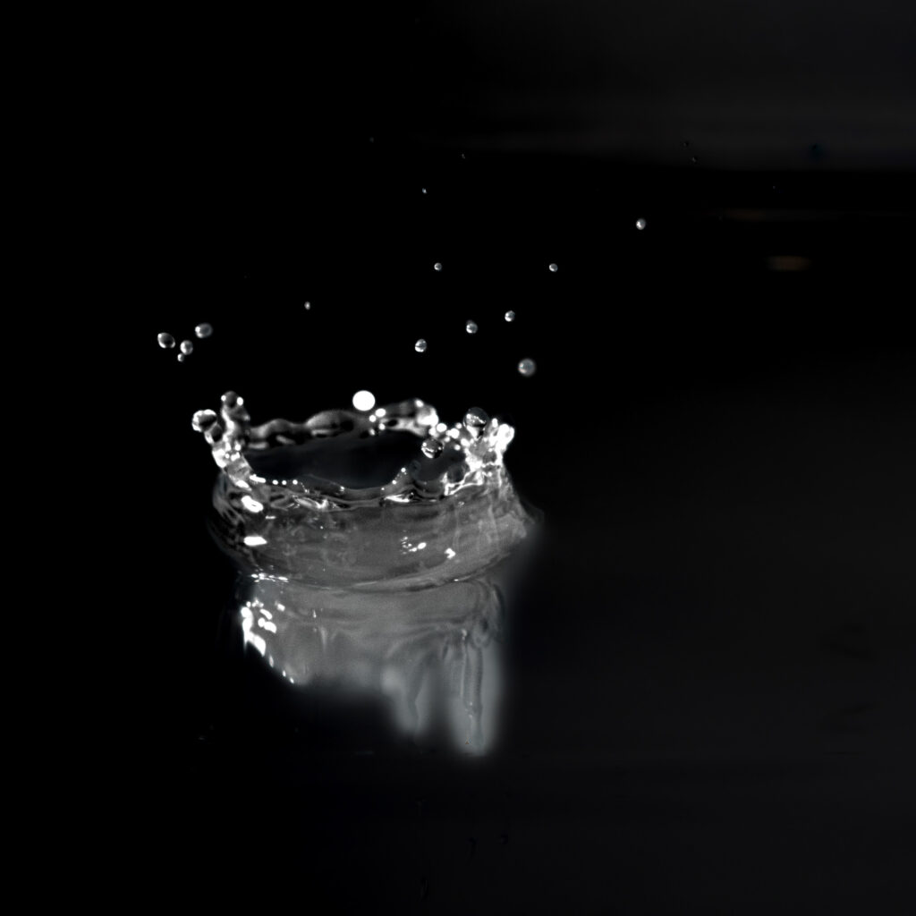 Gros plan sur une goutte d'eau éclaboussant une surface sombre, créant une gerbe en forme de couronne avec des gouttelettes suspendues dans les airs sur un fond noir.